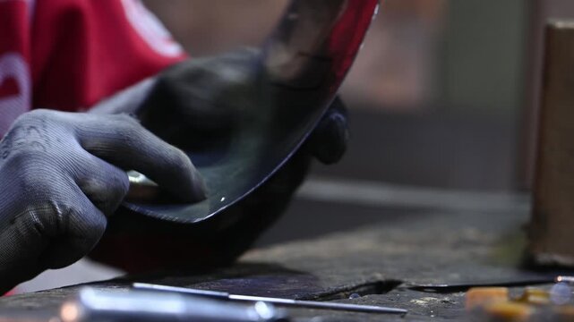 A worker uses a file to remove metal shavings from the edge of a hole in a product. Handmade.