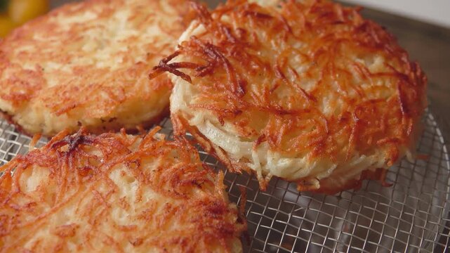 Wooden spatula placing a crispy golden brown potato pancake onto a metal cooling rack. Delicious homemade draniki.