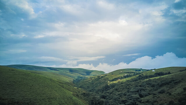Aerial view of rolling green hills and valleys under a vast sky painted with dramatic blues and whites, Obudu, Cross River, Nigeria.