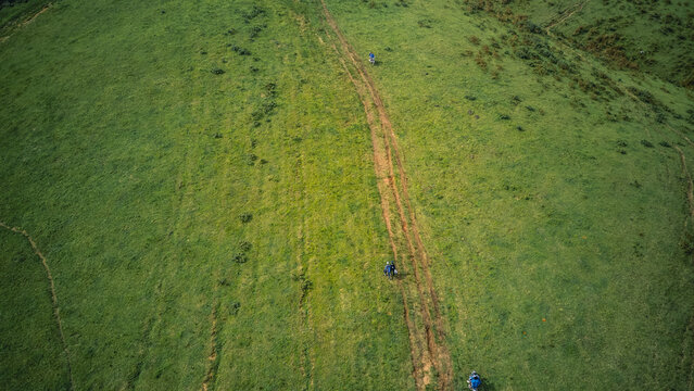 Aerial view of hikers traversing the vibrant green, undulating slopes, their path a stark, earthy ribbon against the lush landscape, Obudu, Cross River, Nigeria.