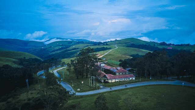 Aerial view of buildings nestled among rolling green hills and winding roads under a twilight sky, Obudu, Cross River, Nigeria.