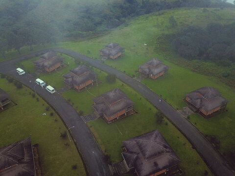 Aerial view of traditional thatched-roof bungalows scattered across a lush green hillside with winding dark roads, Obudu, Cross River, Nigeria.