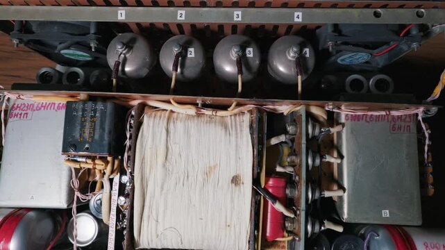 Internal circuitry of a custom-built vacuum tube amplifier. The perspective reveals electronic components including radio tubes, transformers, and hand-labeled wiring in a metal chassis.