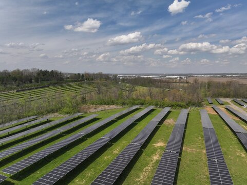 Aerial view of solar panels stretching across the landscape under a blue sky dotted with fluffy clouds, Lebanon, Ohio, United States.