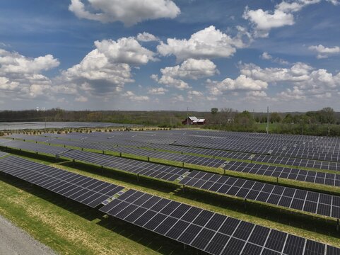 Aerial view of solar panels stretching into the horizon near a distant barn under a sky filled with fluffy clouds, Lebanon, Ohio, United States.
