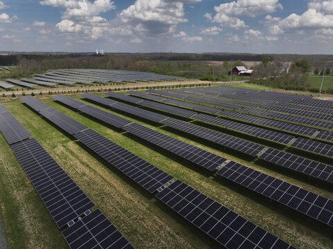 Aerial view of vast solar panel array stretching across the landscape, contrasting with distant trees and buildings, Lebanon, Ohio, United States.
