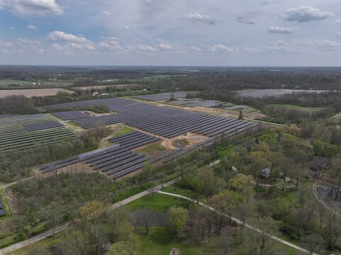 Aerial view of sprawling solar panel arrays glinting under a vast sky, bordered by verdant trees and fields, reflecting a commitment to renewable energy, Lebanon, Ohio, United States.