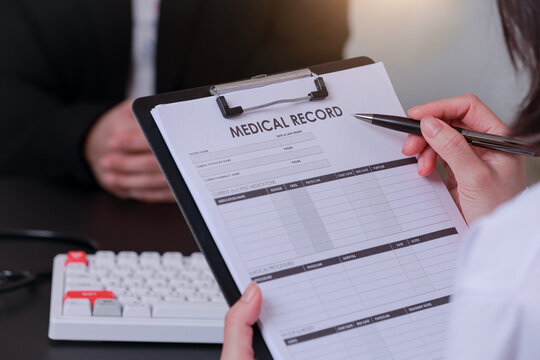 Focused doctor performing medical data entry on clipboard record form during patient consultation at desk clinic office