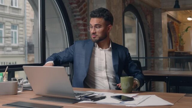 Arabian business man finish computer job listening music relaxing drinking coffee tea satisfied male guy businessman finish laptop using end work happy smiling pause break put on headphones in office