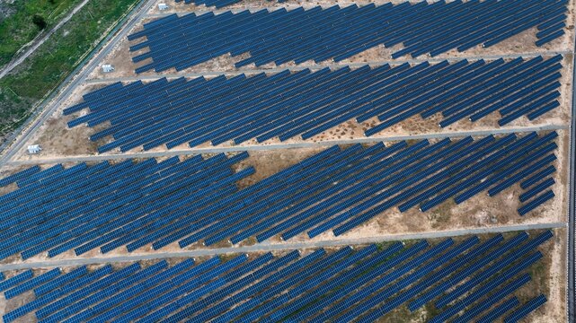 Aerial view of vast, dark blue solar panels stretching across a sun-baked, light brown landscape, contrasting with sparse green patches, Maiduguri, Borno, Nigeria.