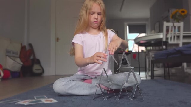 A girl carefully and patiently building a card house. The cards keep falling down. Game concentration attention focus.