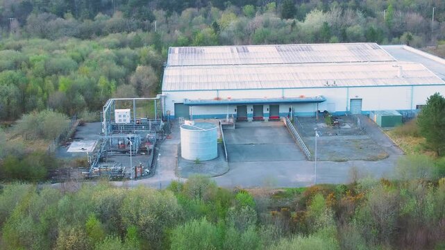 Medium Aerial View Over Run Down Warehouse with Loading Bays Surrounded by Forest Landscape. Industrial Infrastructre Surrounded by Natural Environment. 4K.