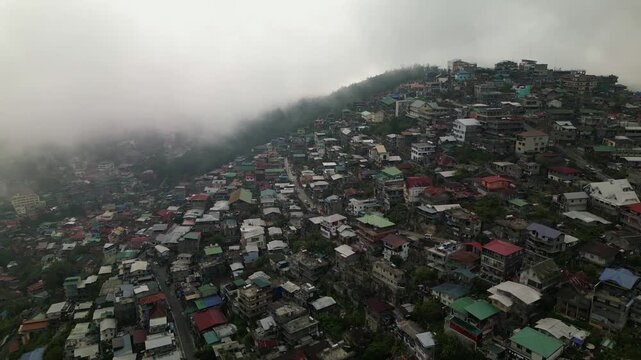 Aerial orbit capturing tightly packed hillside homes as fog blankets parts of Quirino Hill in Baguio City, Philippines.