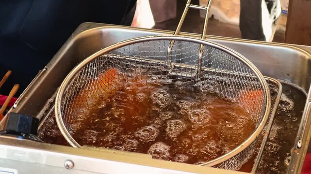 A close-up of food being deep-fried in hot oil using a deep-frying basket. Concept for street food and fast food. High quality 4k footage