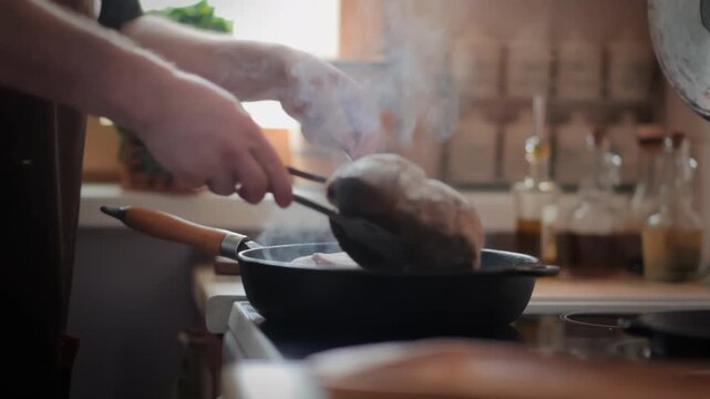 A man flips a sizzling Osso Buco steak on a hot grill pan. Spices and herbs are blurred in the background. Concept of gourmet home cooking