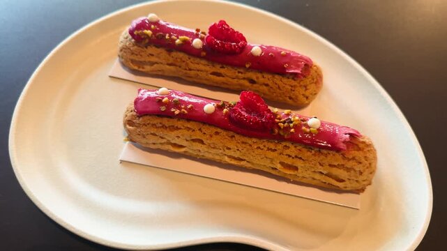 Elegant French eclairs with raspberry glaze and creamy filling served on a stylish plate. Close-up shot highlighting delicate texture, vibrant colors and gourmet presentation, perfect for bakery