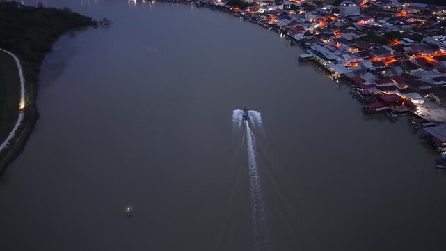 Drone captures fishing boat on Sungai Udang river near illuminated riverside houses at night.