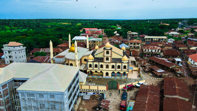 Aerial view of a prominent golden-domed mosque with minarets, nestled among dense red-roofed buildings and green trees, Igbaja, Nigeria.