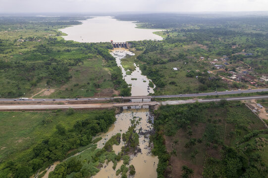 Aerial view of the muddy river cutting through verdant forests and the town, with a bridge standing firm, Asejire, Oyo, Nigeria.