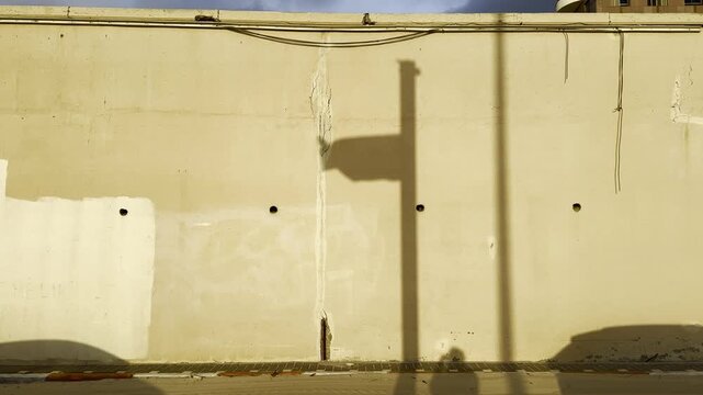 Shadow of a waving flag cast on a yellow plastered wall, creating a dynamic abstract pattern formed by wind and light.