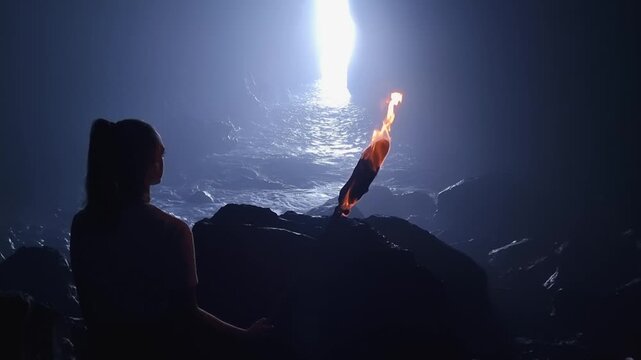 Woman sitting in a meditation pose, looking at a burning torch in a dark, mysterious cave with misty water and dramatic light