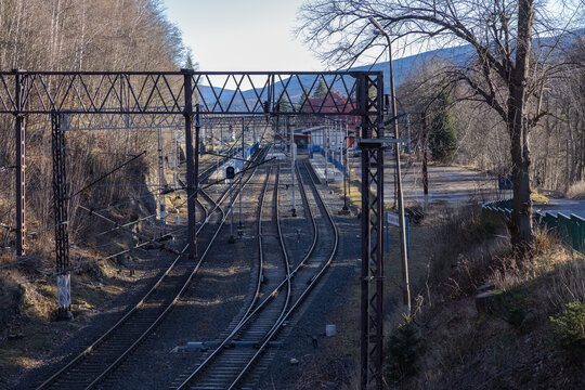 Railway tracks lead toward a remote mountain station with overhead catenary lines on a clear sunny day, perfectly symbolizing modern infrastructure, travel connectivity, and scenic landscape journeys