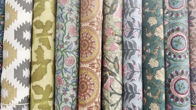 Vertical rolls of colorful fabric with various traditional ethnic and floral patterns stacked together.
