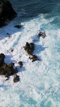 Aerial view of foamy sea waves breaking on the rocky coast of Los Gigantes, Tenerife, Canary Islands, Spain.