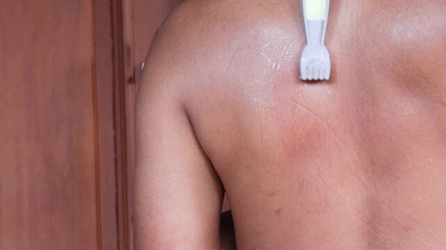 An Asian man scratches his back to relieve an itch with a back scratcher.