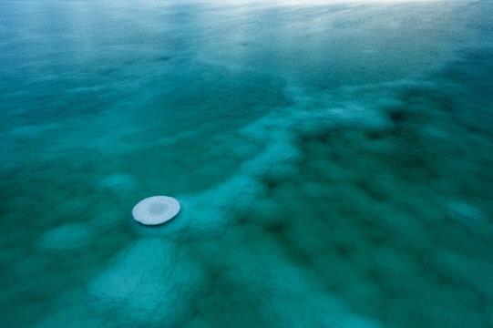 Aerial view of the Dead Sea's turquoise waters swirl around a solitary circular structure, creating a mesmerizing contrast of textures and tones, Israel.