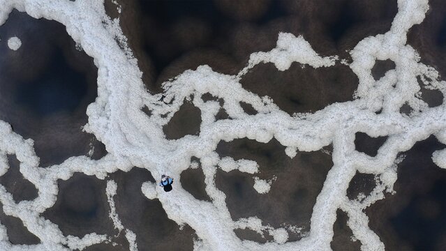 Aerial view of a lone figure traversing a mesmerizing labyrinth of brilliant white salt patterns against the deep, dark waters, Dead Sea, Israel.