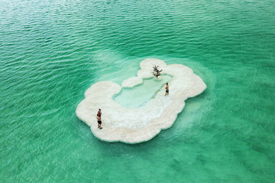 Aerial view of dramatic white salt formations, resembling a sculpted cloud, emerge from the vivid emerald waters, creating a serene pool where figures relax, Ein Bokek, Israel.