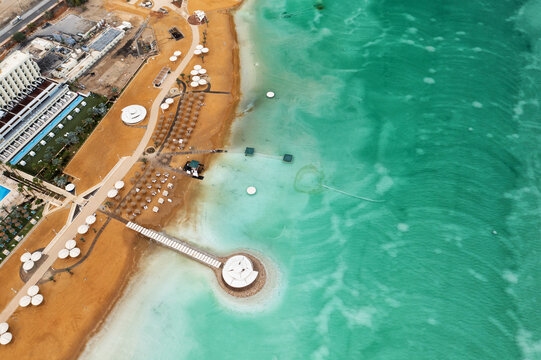 Aerial view of a vibrant Dead Sea resort, golden sands and white parasols meet the striking turquoise waters, Ein Bokek, Israel.