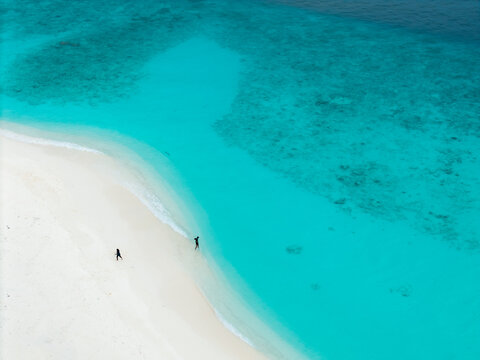 Aerial view of turquoise waters meet the pristine white sands, where tiny figures stroll along the shore, Hoarafushi, Thiladhunmathee Uthuruburi, Maldives.