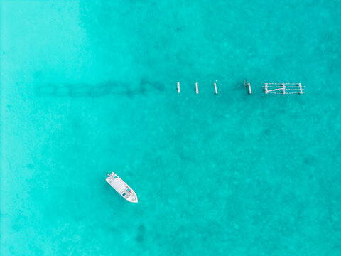 Aerial view of a solitary white boat on dazzling turquoise waters, with dark underwater structures visible, Hoarafushi, Thiladhunmathee Uthuruburi, Maldives.