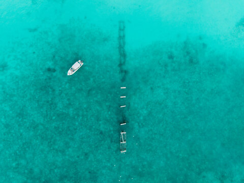 Aerial view of a solitary white boat gracefully drifting over crystal-clear turquoise waters, revealing a haunting submerged structure below, Hoarafushi, Thiladhunmathee Uthuruburi, Maldives.