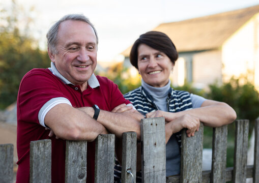 Happy married elderly couple have conversation near the fence of their farm