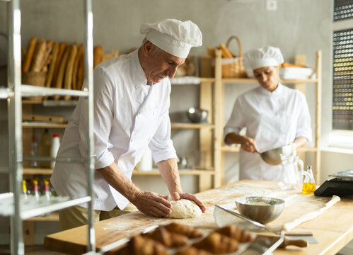 Man and woman, experienced bakers, prepare dough for baguettes and croissants together in private bakery