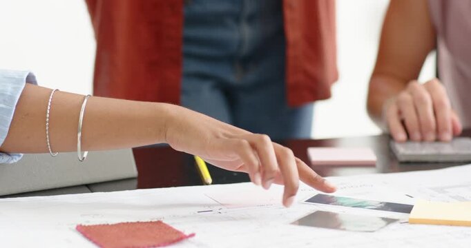 Diverse female team following hands pointing, tapping mockups and selecting fabrics at design table