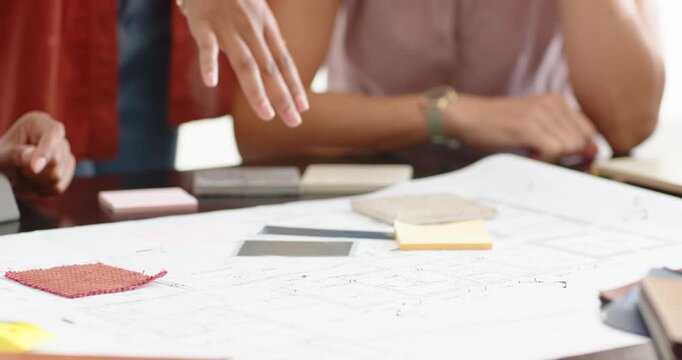 Diverse coworkers choosing materials from plans, curly woman reaching in and pointing at red swatch