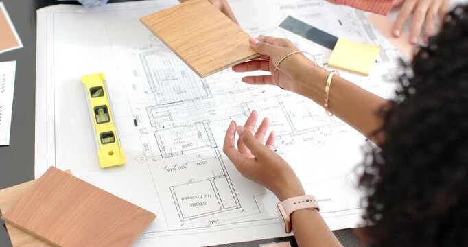 Diverse women offering wood sample pointing at plans in office with green pencil choosing finish