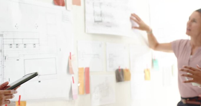 Diverse female team at studio pinboard reviewing plans after tablet tap and pointing, copy space