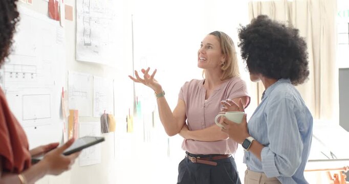 Diverse female team at wall, presenter in pink blouse responding to pinned plans, explaining layout