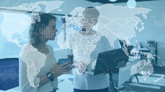 Female coworkers working in open office, holding blue mug and pointing to laptop with map overlay