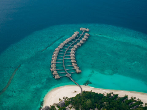 Aerial view of a luxurious overwater resort curving gracefully from a vibrant green island into the sparkling turquoise sea, Hoarafushi, Thiladhunmathee Uthuruburi, Maldives.