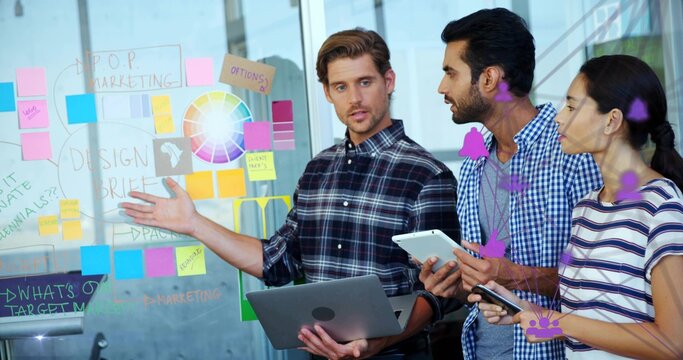 Gesturing presenter wearing plaid shirt holding laptop and pointing at glass wall with sticky notes