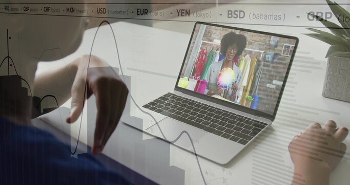 Reaching client in blue top adjusting charts at desk, laptop showing color wheel, currency overlay