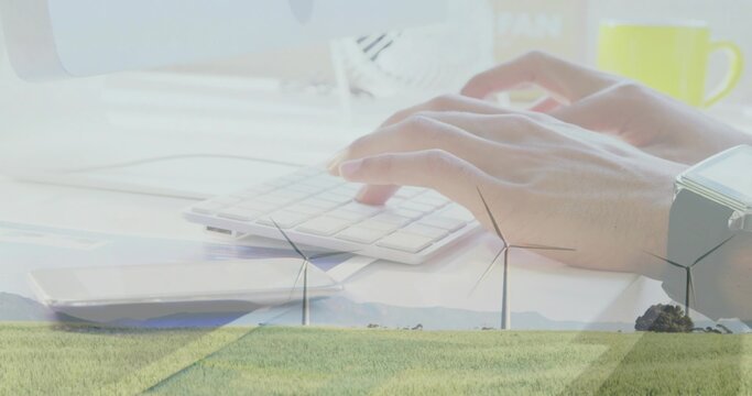 Typing adult hands resting on small keyboard at pale desk, merging with wind turbines, mug, watch