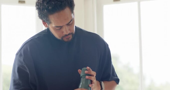 African American man twisting bottle cap, checking opening, sipping, hydrating at home by window