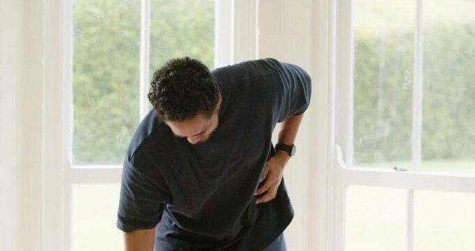 African American man lowering weight bending and pressing right flank in windowed room easing cramp